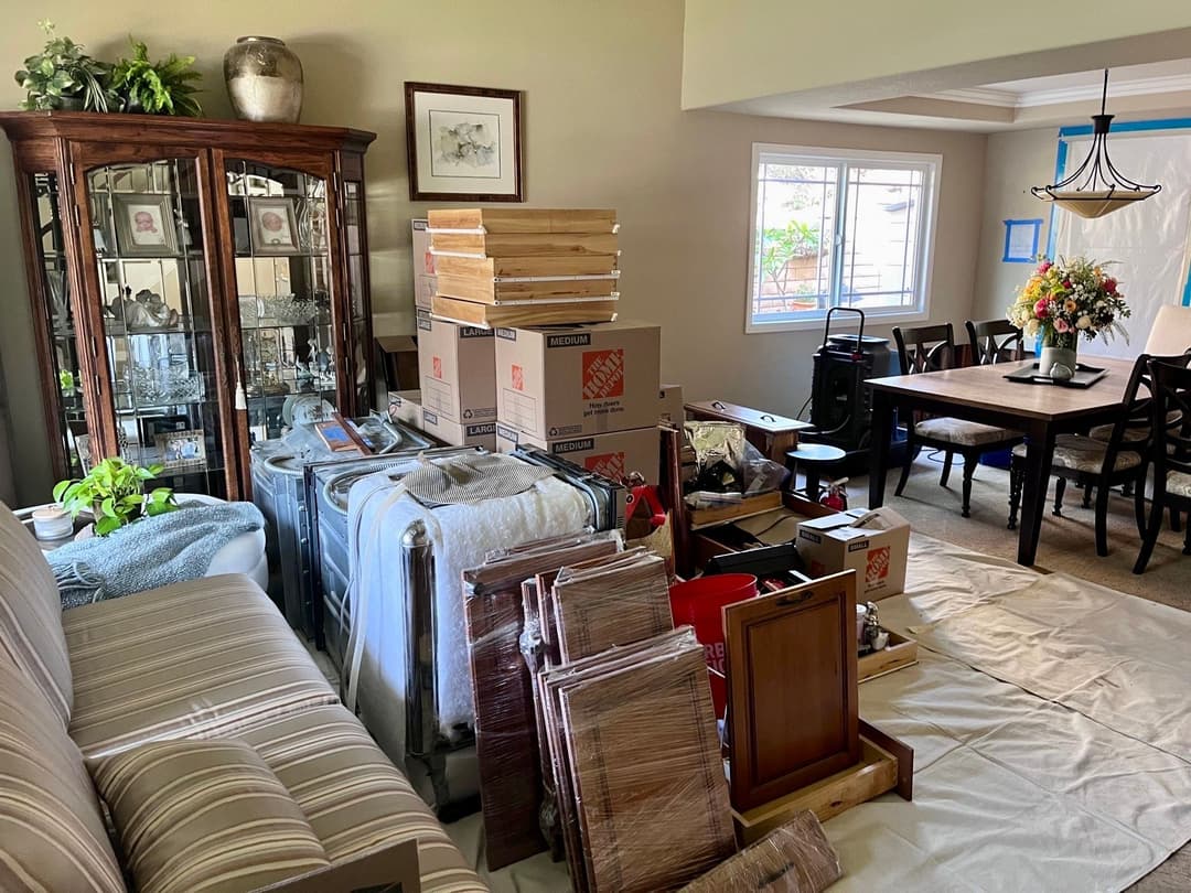 Cluttered living room with moving boxes, packing materials, and home furnishings in disarray.