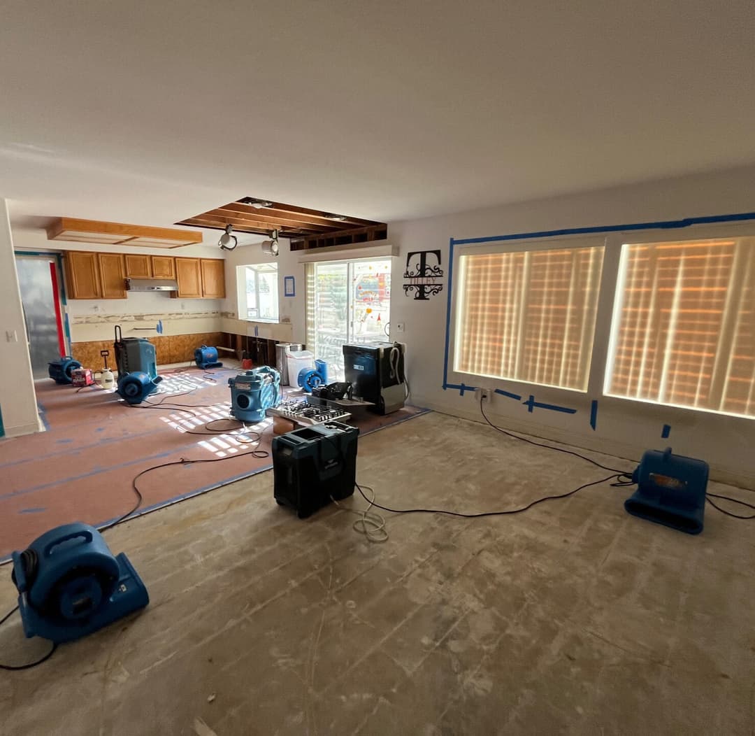 Water damage restoration with blue drying fans and a partially renovated kitchen in view.