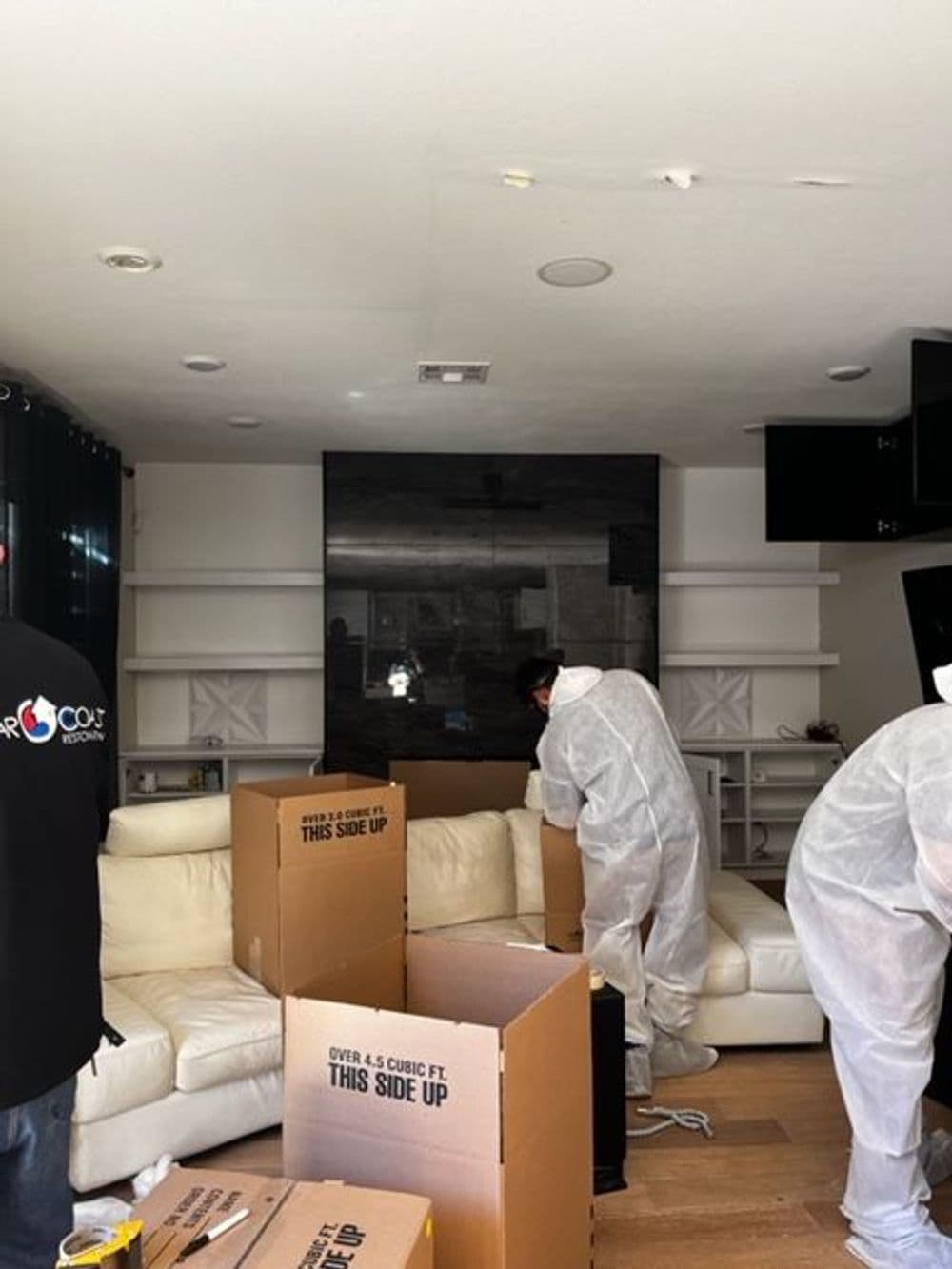 Workers in protective gear packing boxes in a living room with a modern design.