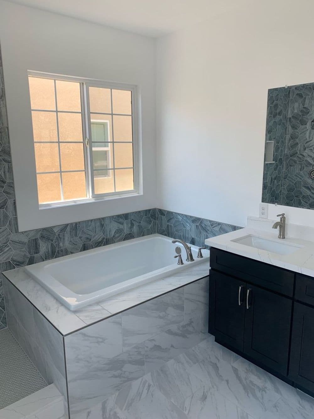 Modern bathroom featuring a soaking tub, dark cabinetry, and elegant tiled walls.