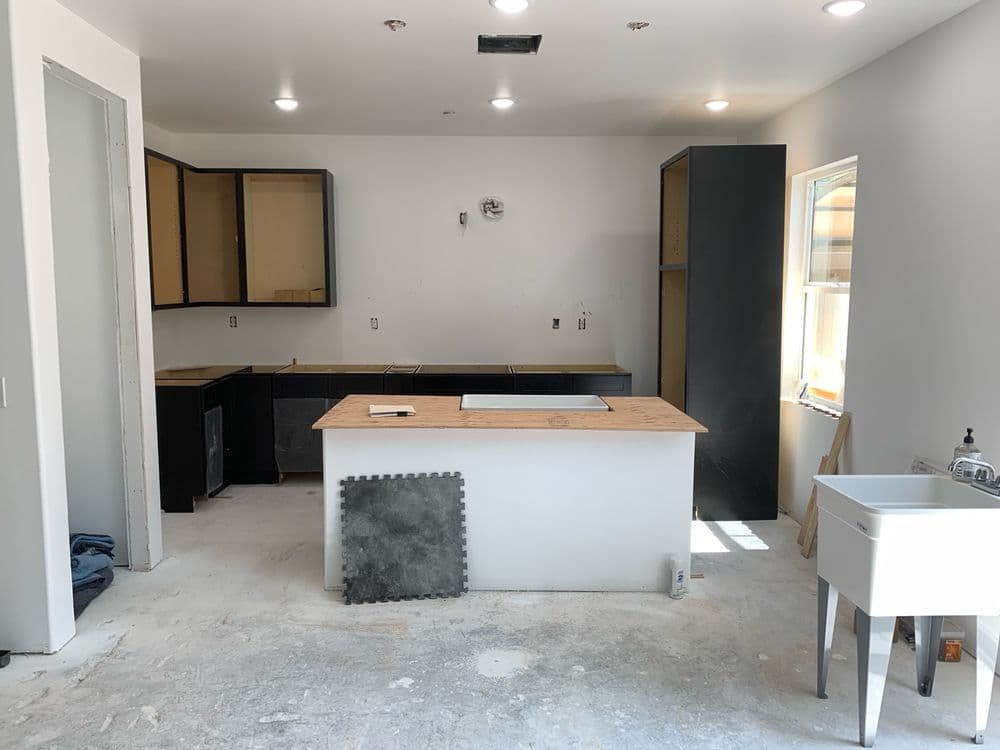 Modern kitchen renovation with unfinished cabinets, countertops, and a farmhouse sink.