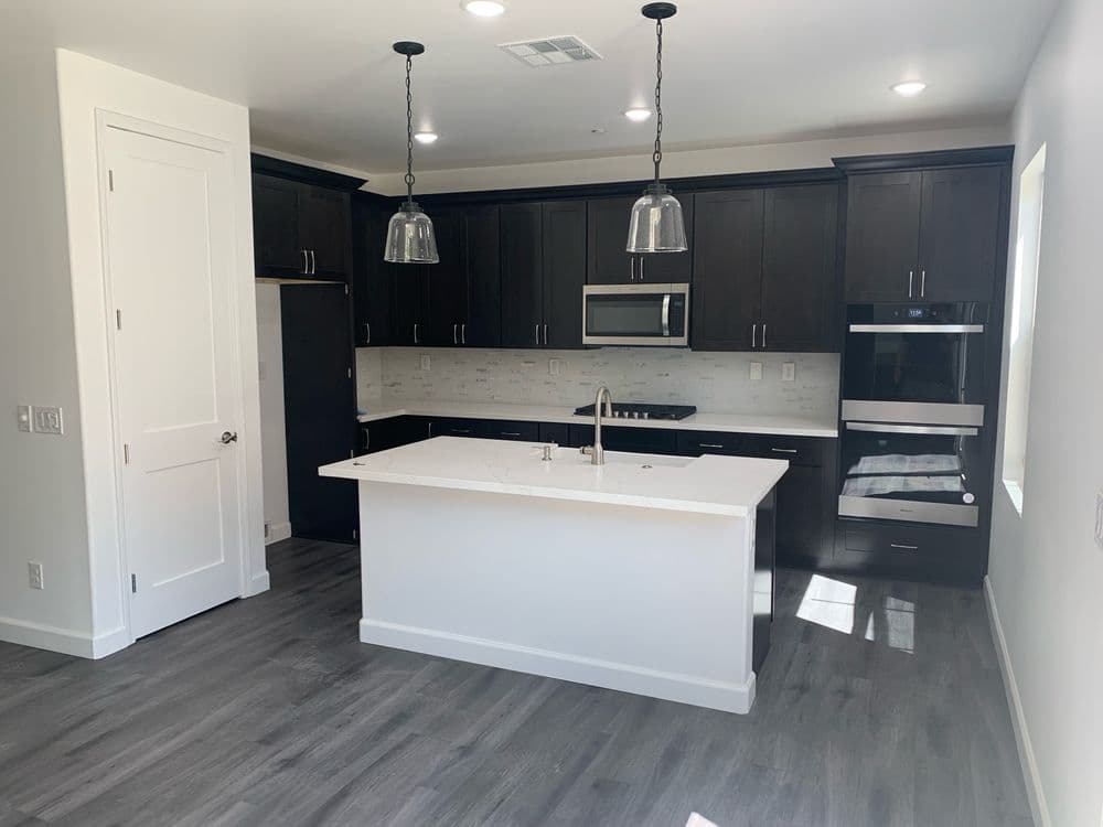 Modern kitchen with dark cabinetry, white island, and stainless steel appliances, bright natural light.