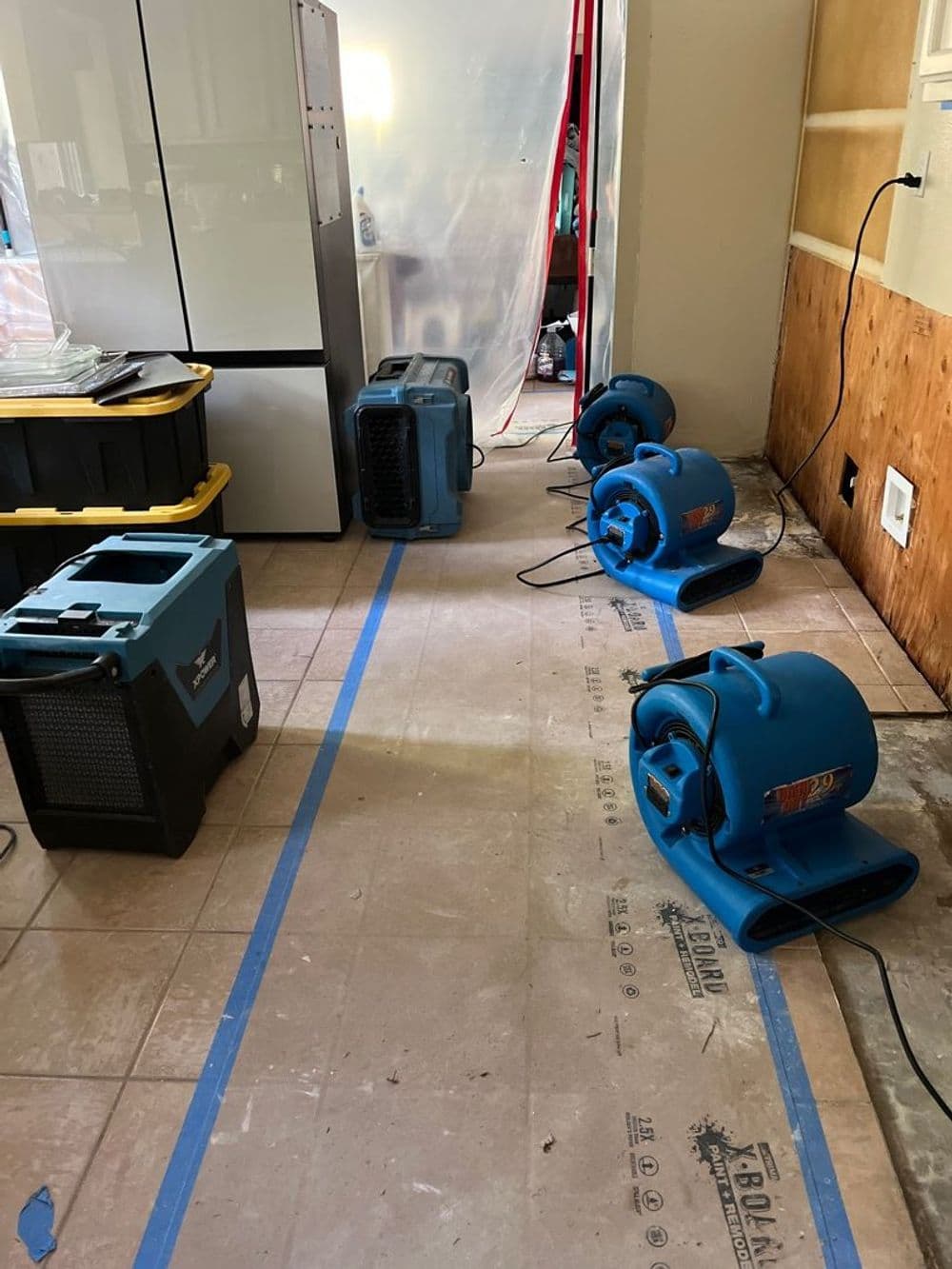 Blue industrial fans and dehumidifiers in a home renovation project drying wet flooring.