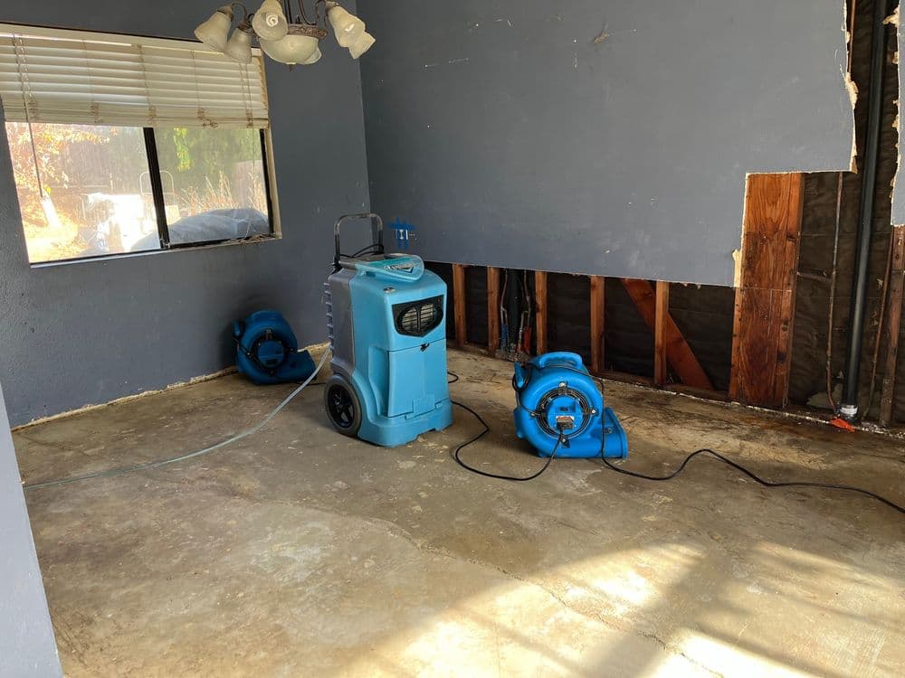 Water damage cleanup equipment in a partially renovated room with exposed walls.