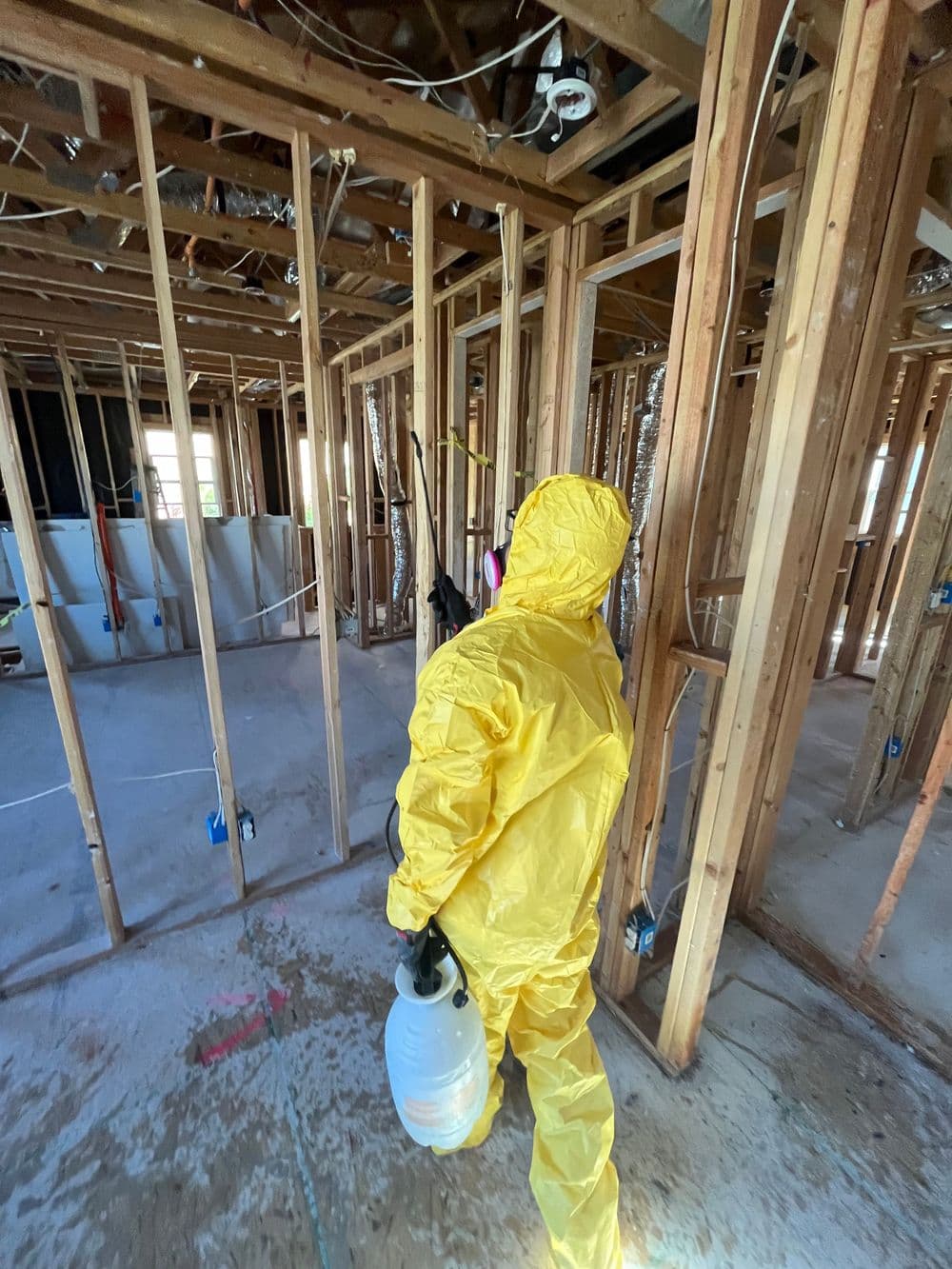 Person in yellow protective suit disinfecting interior of a home under renovation.
