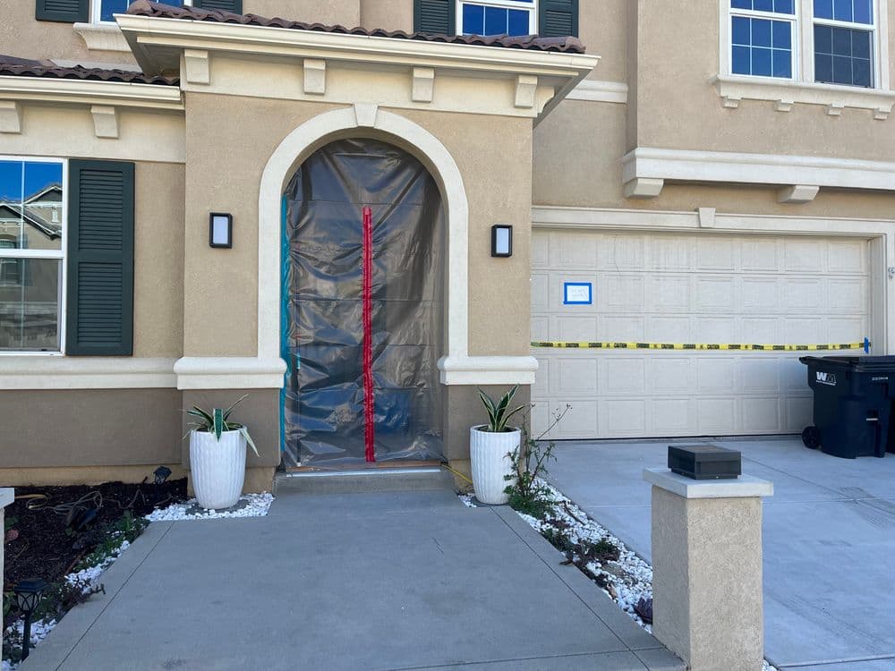 Front entryway of a house with plastic covering, caution tape, and potted plants.
