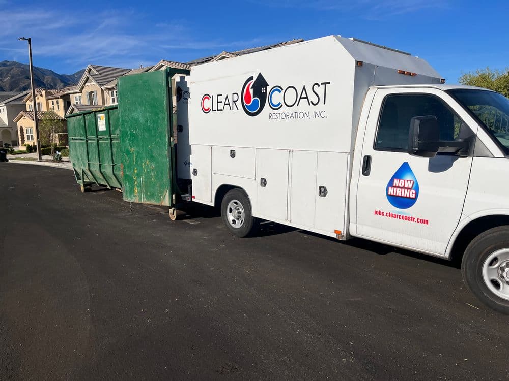 Clear Coast Restoration truck with green dumpster parked on residential street. Now hiring.