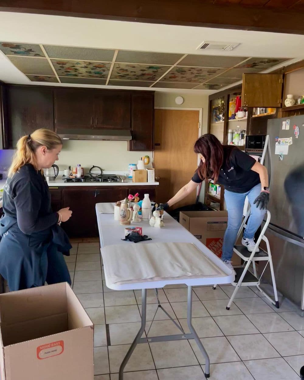 Two women organizing kitchen items on a table while preparing for packing and moving.