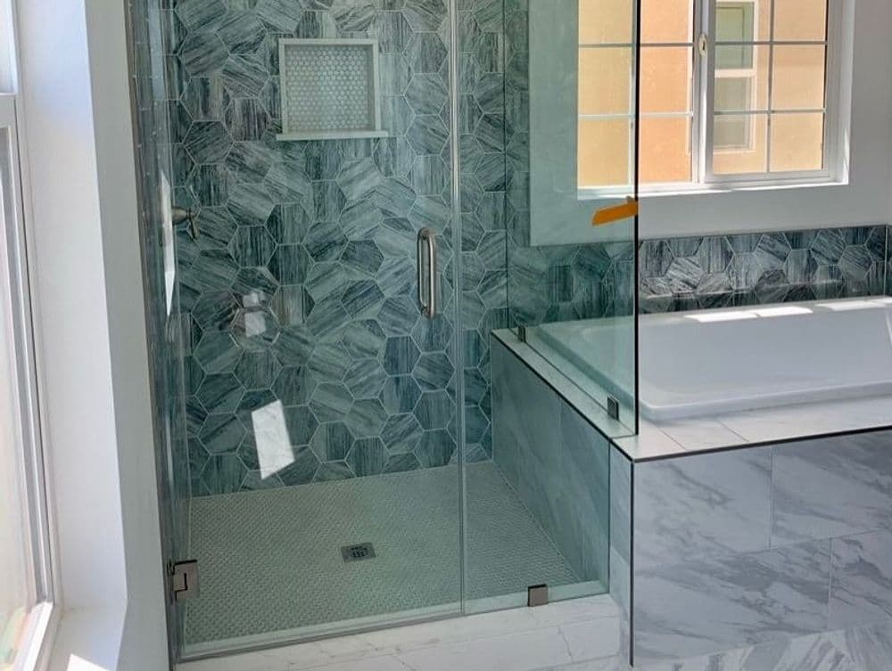 Modern bathroom featuring a glass shower enclosure, hexagonal tile walls, and a freestanding tub.