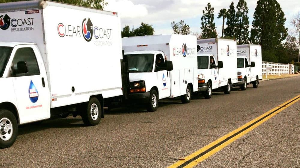 Fleet of Clear Coast Restoration trucks parked along a road under a cloudy sky.